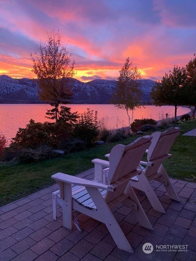 patio terrace at dusk featuring a water and mountain view and a lawn