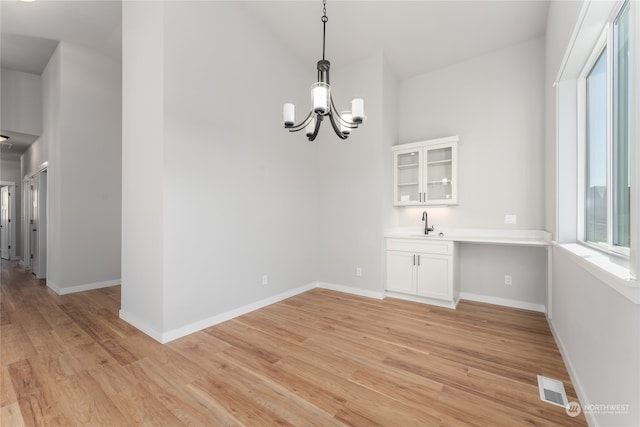 unfurnished dining area with a notable chandelier, sink, and light wood-type flooring