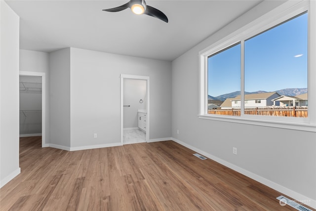 unfurnished bedroom with connected bathroom, a mountain view, a walk in closet, light hardwood / wood-style floors, and ceiling fan