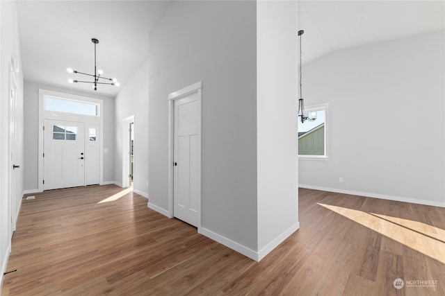 entryway with lofted ceiling, wood-type flooring, and an inviting chandelier