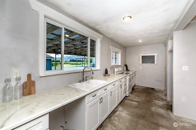 kitchen with white electric range, sink, light stone counters, white cabinetry, and concrete floors