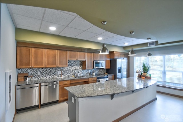 kitchen with light stone countertops, decorative backsplash, a kitchen breakfast bar, stainless steel appliances, and hanging light fixtures