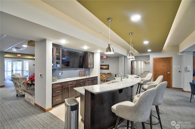 kitchen featuring a breakfast bar, light carpet, sink, hanging light fixtures, and an island with sink