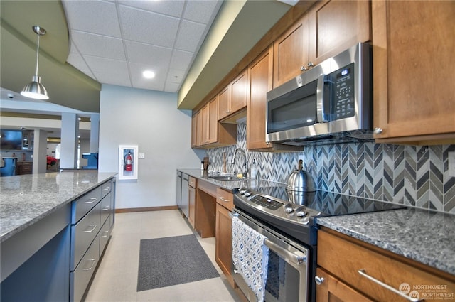 kitchen featuring decorative backsplash, appliances with stainless steel finishes, a paneled ceiling, dark stone counters, and sink