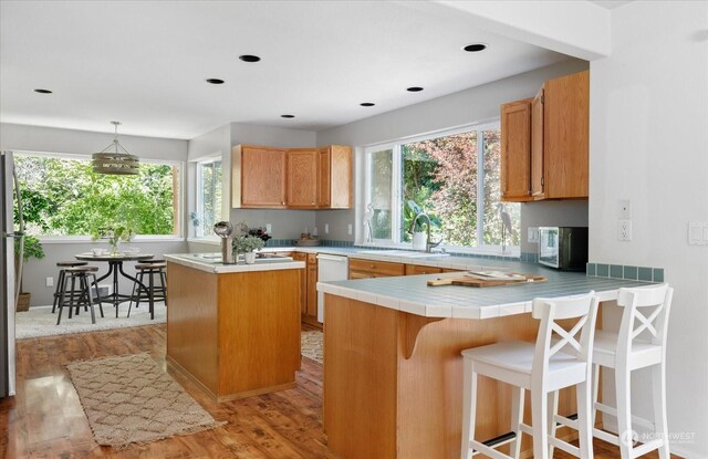 kitchen featuring sink, dishwasher, light hardwood / wood-style floors, decorative light fixtures, and kitchen peninsula