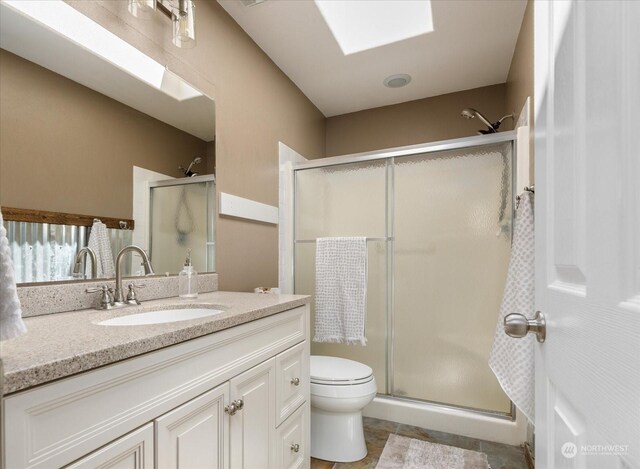 bathroom featuring an enclosed shower, vanity, toilet, and a skylight