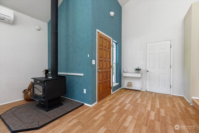 entryway with hardwood / wood-style flooring, an AC wall unit, a wood stove, and high vaulted ceiling