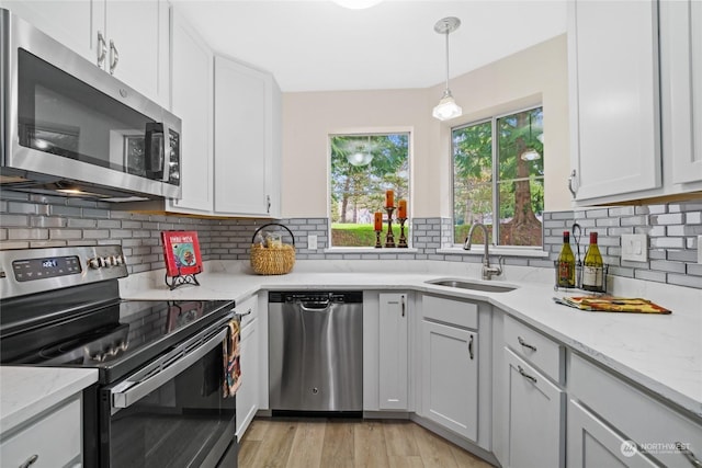 kitchen with appliances with stainless steel finishes, sink, white cabinets, hanging light fixtures, and light stone countertops