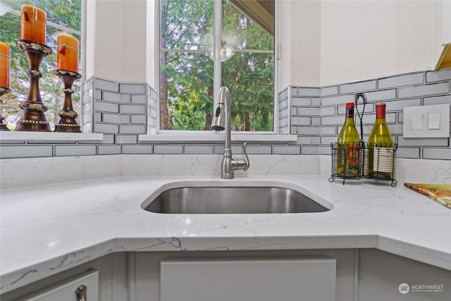 details featuring white cabinetry, light stone countertops, sink, and backsplash