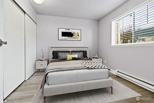 bedroom with a baseboard radiator, a closet, and light hardwood / wood-style flooring