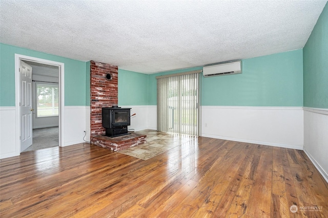 unfurnished living room featuring a wood stove, a textured ceiling, hardwood / wood-style flooring, and a wall unit AC