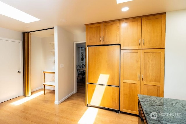 kitchen featuring paneled refrigerator, light hardwood / wood-style floors, and dark stone countertops