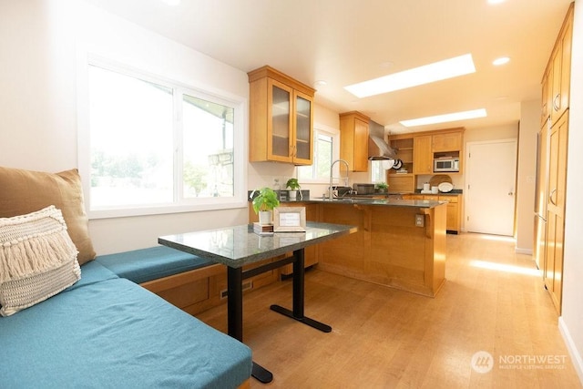 kitchen with sink, a kitchen breakfast bar, kitchen peninsula, wall chimney range hood, and light wood-type flooring