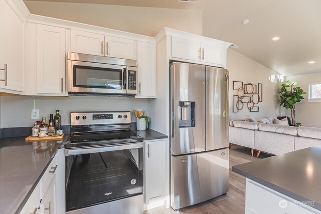 kitchen with light wood-type flooring, appliances with stainless steel finishes, vaulted ceiling, and white cabinets