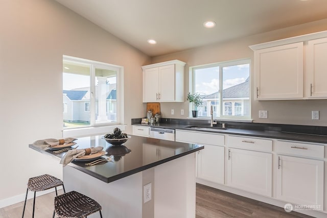 kitchen with dark countertops, a breakfast bar, a sink, white cabinetry, and stainless steel dishwasher