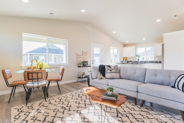 living area featuring light wood-style floors, lofted ceiling, baseboards, and recessed lighting