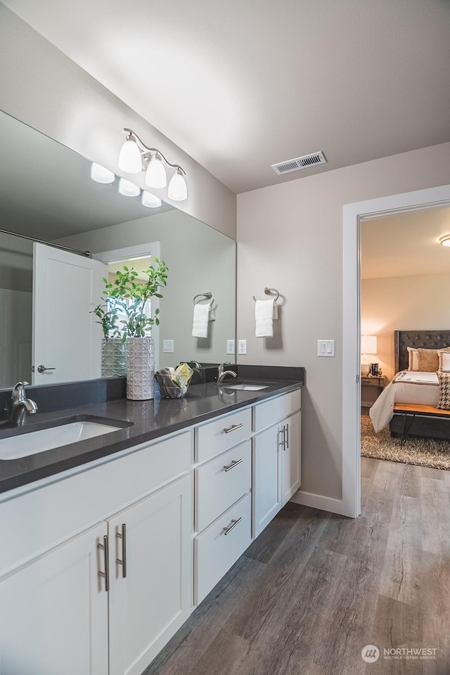 ensuite bathroom with a sink, visible vents, connected bathroom, and wood finished floors