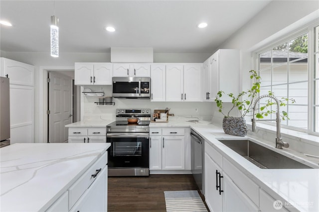 kitchen with a sink, appliances with stainless steel finishes, white cabinets, and light stone counters