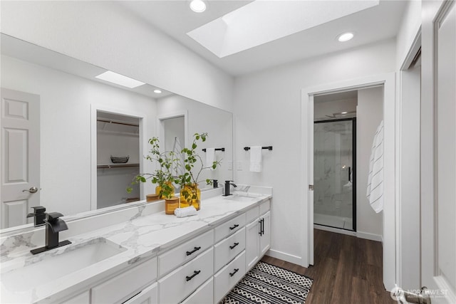 bathroom featuring double vanity, wood finished floors, a shower stall, a sink, and a skylight