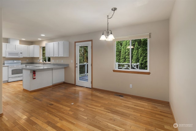 kitchen with hanging light fixtures, white cabinets, light wood-type flooring, white appliances, and a peninsula