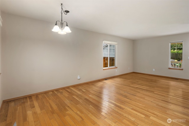 unfurnished room with light wood-style floors, a notable chandelier, and baseboards