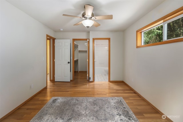 unfurnished bedroom featuring a walk in closet, ceiling fan, light wood-style flooring, and baseboards