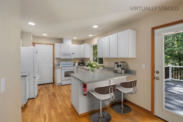 kitchen featuring a peninsula, white appliances, a breakfast bar, light wood-type flooring, and white cabinetry