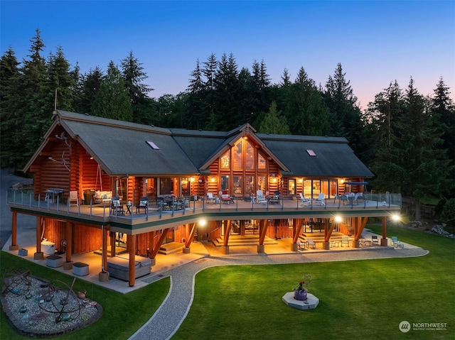 back house at dusk featuring a lawn, a balcony, and a patio