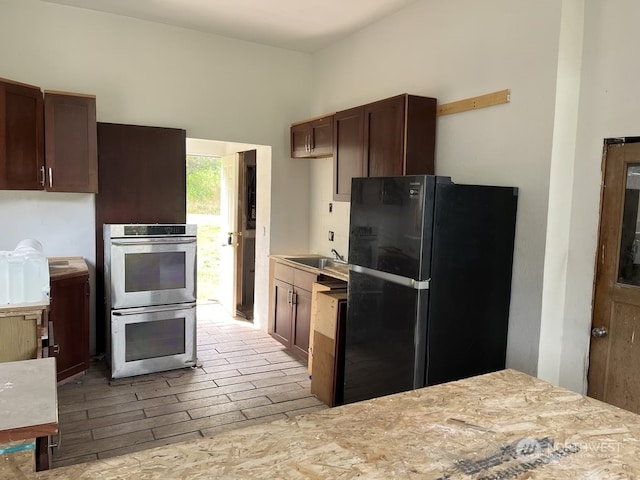 kitchen featuring range, black refrigerator, stainless steel double oven, dark brown cabinetry, and sink