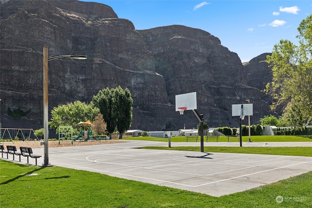 view of sport court featuring a mountain view, a playground, and a lawn