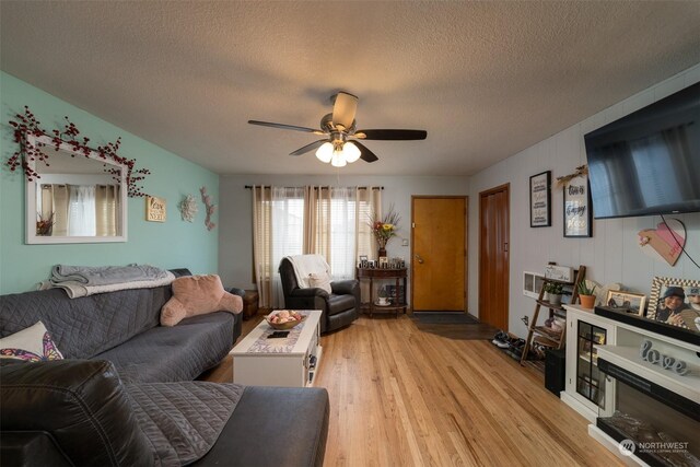 living room with light hardwood / wood-style flooring, a textured ceiling, and ceiling fan