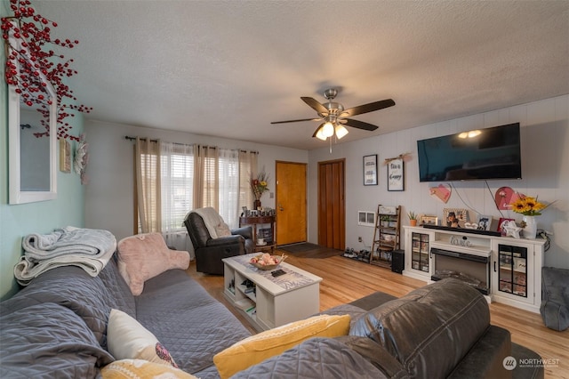 living room featuring ceiling fan, light hardwood / wood-style flooring, and a textured ceiling