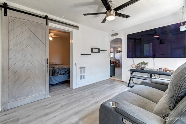 living room with light wood-type flooring, ceiling fan, and a barn door