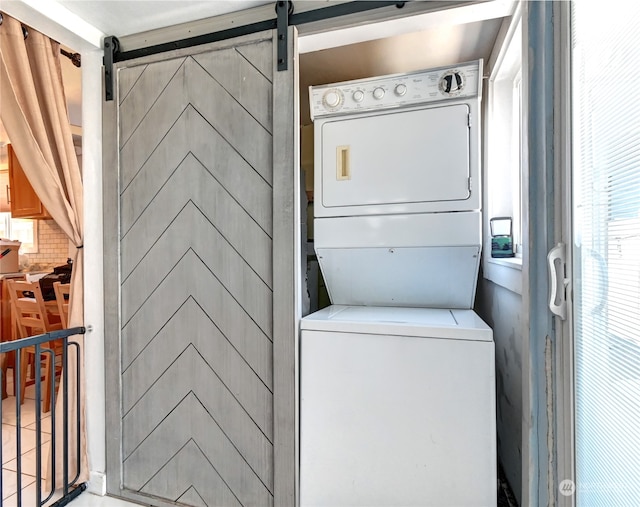 clothes washing area featuring stacked washing maching and dryer and a barn door