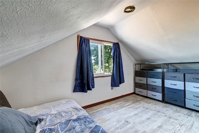 bedroom featuring vaulted ceiling, light wood-type flooring, and a textured ceiling