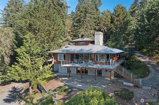 view of front of home with a standing seam roof, metal roof, a patio, stairway, and a chimney