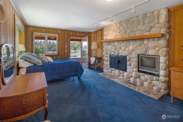 bedroom with access to outside, a stone fireplace, carpet floors, and wooden walls