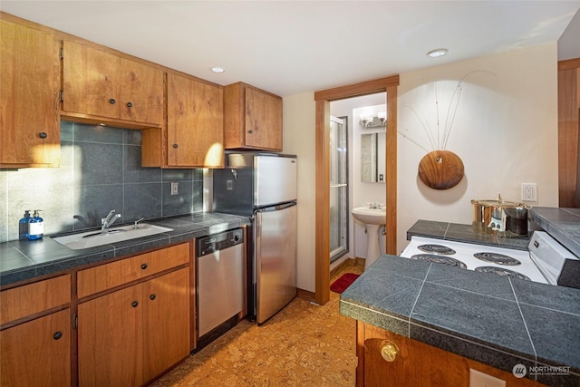 kitchen featuring brown cabinets, tile countertops, stainless steel appliances, backsplash, and a sink