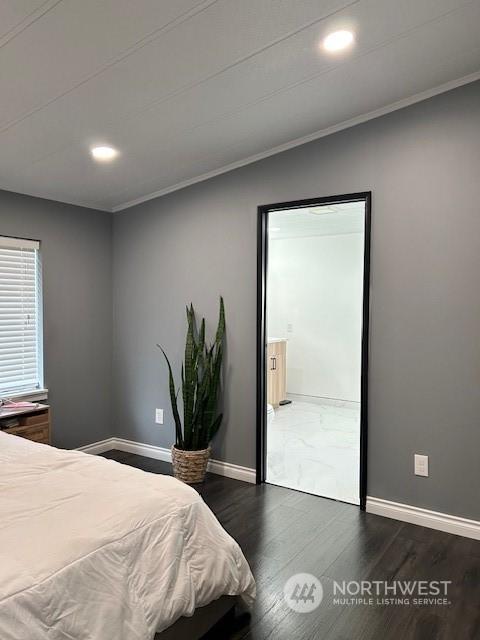 bedroom with connected bathroom, dark hardwood / wood-style flooring, and ornamental molding