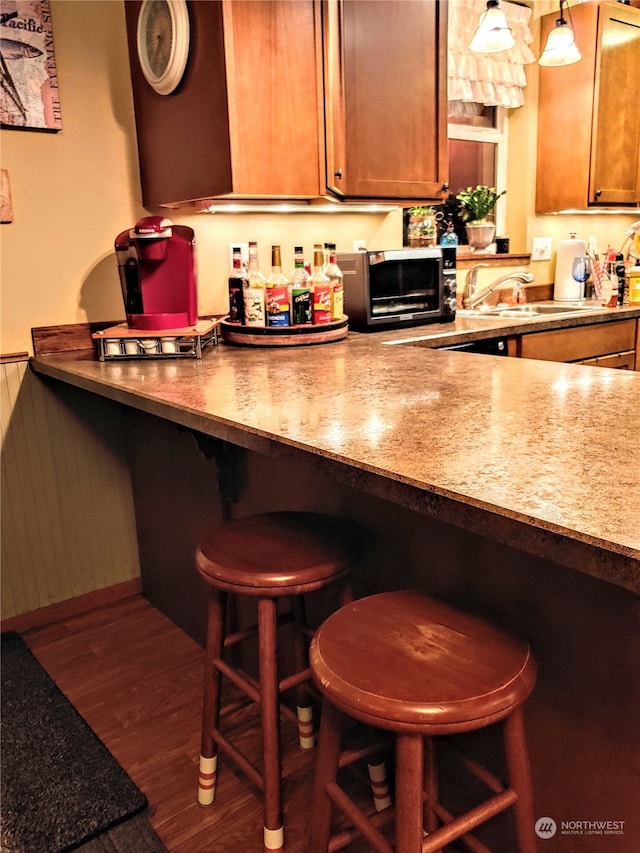 kitchen with sink, dark hardwood / wood-style floors, pendant lighting, and a kitchen breakfast bar