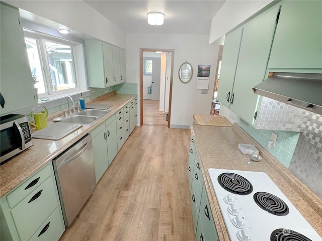 kitchen featuring light wood-type flooring, green cabinets, appliances with stainless steel finishes, decorative backsplash, and sink