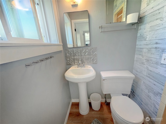 bathroom with a wealth of natural light, wooden walls, hardwood / wood-style flooring, and toilet