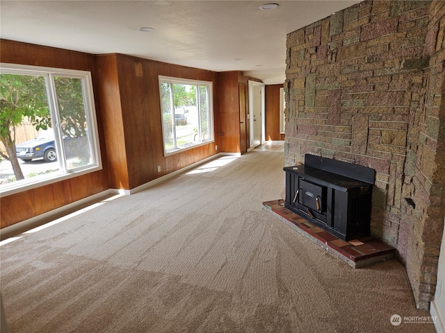 unfurnished living room with wooden walls, light colored carpet, and a wood stove