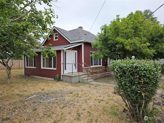 bungalow-style home with a shingled roof, fence, and a chimney