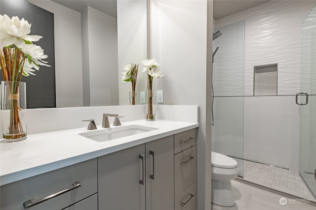 bathroom with a shower with door, vanity, tile patterned flooring, and toilet