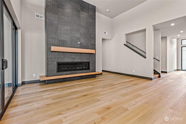 unfurnished living room featuring baseboards, stairway, wood finished floors, and a large fireplace