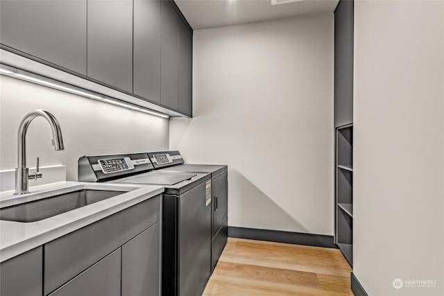 washroom featuring light wood finished floors, a sink, cabinet space, and separate washer and dryer
