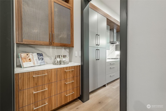interior space with light countertops, light wood-style floors, wall chimney range hood, modern cabinets, and glass insert cabinets