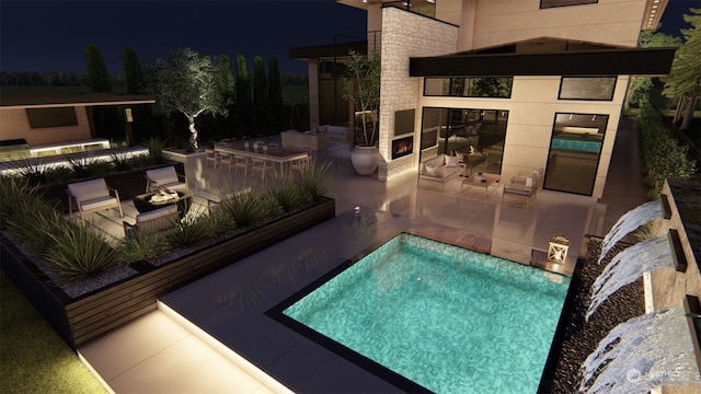 pool at night featuring exterior kitchen, a patio area, and a bar