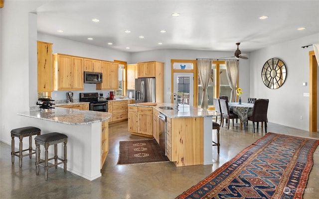 kitchen featuring light brown cabinetry, sink, appliances with stainless steel finishes, a kitchen breakfast bar, and light stone countertops